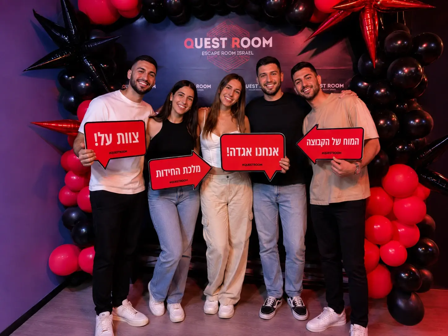 קבוצת חברים מצטלמת בלובי Quest Room אחרי משחק בחדר בריחה