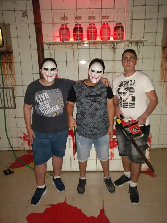 שלושה משתתפים עם מסכות ואביזר מסור בחדר האימה